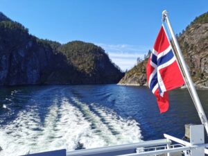 The cruise boats negotiate the narrow passages of the fjord with the Norwegian flag fluttering in the cool breeze
