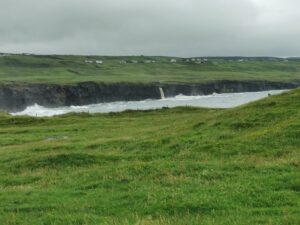 The wild sea, the waterfall flows over the cliffs, the houses on the Cliffs of Moher