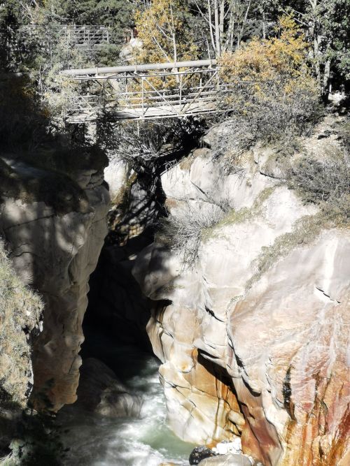The Bhagirathi River squeezes through a gap in the rocks, a small bridge spans the space between