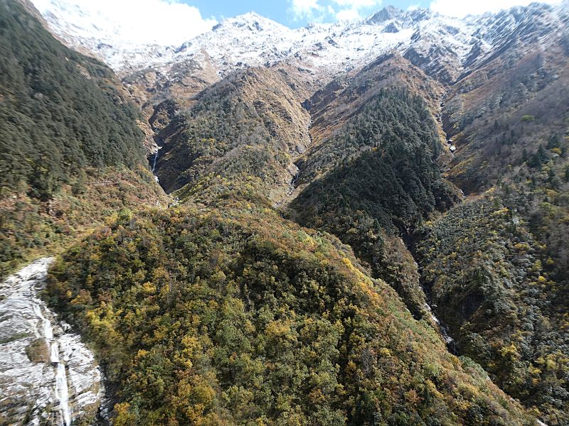 The wide view of fresh snow, high mountains, small waterfalls and autumn colours in the moutains to the side of Yamunotri Temple complex