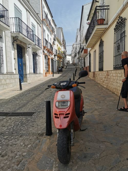 A narrow street in Ubrique with Juliet balconies and coloured doors, cobblestones and a small bike