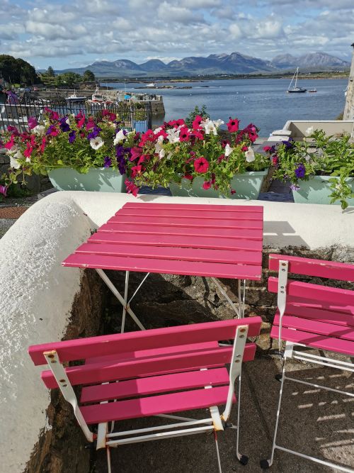 Pink table and chairs with colourful flowers overlooking the harbour in Roundstone